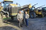 Two men standing in front of agricultural field equipment